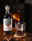 Glass of Devon Rum Co Coffee Rum Liqueur with a bottle and coffee beans in front of a fireplace.