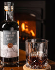Glass of Devon Rum Co Coffee Rum Liqueur with a bottle and coffee beans in front of a fireplace.