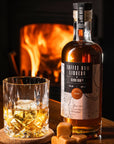 Glass of Devon Rum Co Toffee Rum Liqueur with a bottle in front of a fireplace