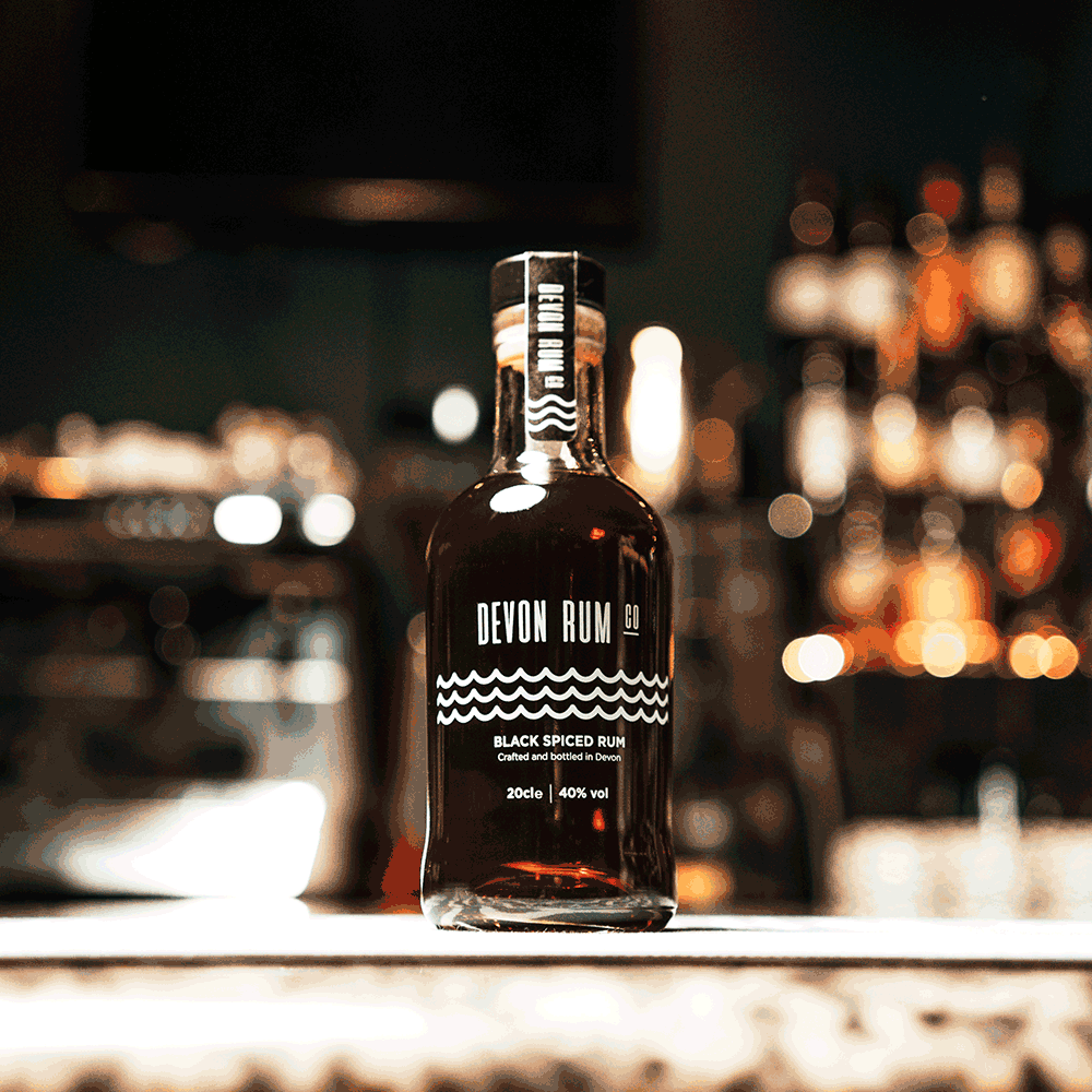 Devon Rum Co Black Spiced Rum with a rum bar behind it.
