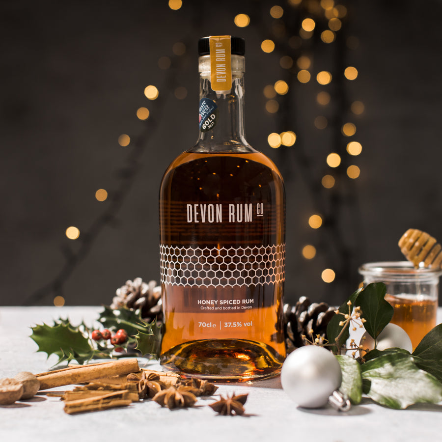 Bottle of Devon Rum Co Honey Spiced Rum with festive decorations on a dark background with fairy lights.