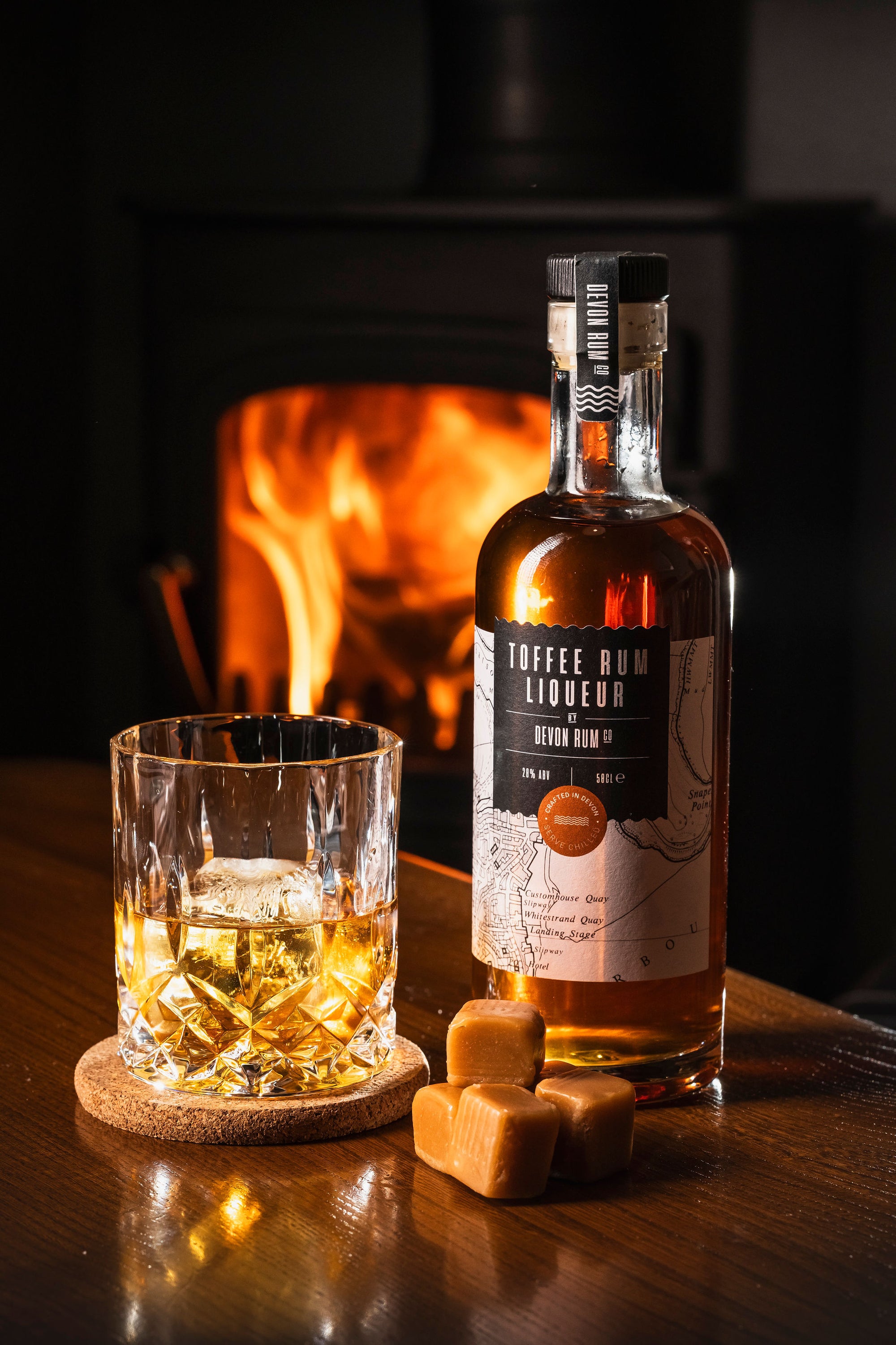 Glass of Devon Rum Co Toffee Rum Liqueur with a bottle in front of a fireplace