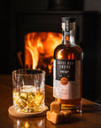 Glass of Devon Rum Co Toffee Rum Liqueur with a bottle in front of a fireplace